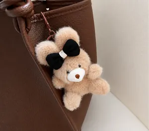 Detailed view of a cute brown plush bear charm attached to a brown faux leather tote bag