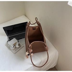 Detail of brown litchi leather bucket bag with knotted strap and small teddy charm
