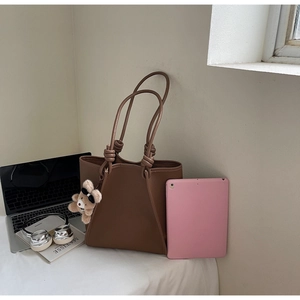 Brown leather tote bag showing large capacity with laptop and cute bear charm accessory
