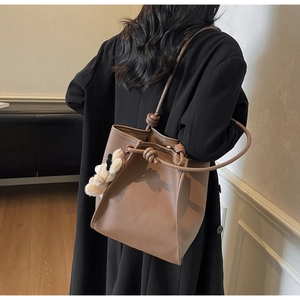 Brown lychee leather tote bag on shoulder with cute cream plush bear pendant
