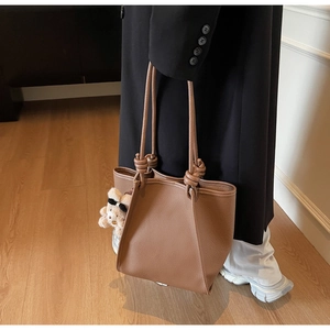 Close-up of brown pebbled leather tote bag featuring unique knotted handles and a cute bear charm