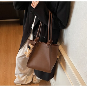 Detail of dark brown leather tote bag with knotted strap and cute bear keychain charm