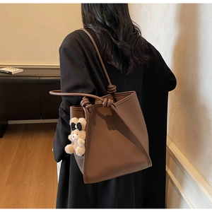 Detail of dark brown pebbled leather tote bag with a cute plush bear charm on the strap