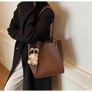 Detail of brown litchi pattern leather tote bag featuring a cute teddy bear charm