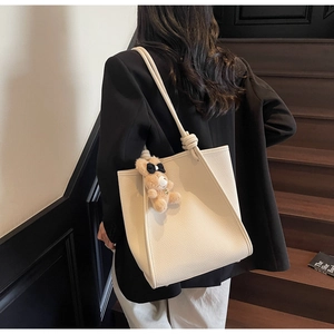 Close-up of cream lychee texture leather tote bag with cute bear charm on shoulder