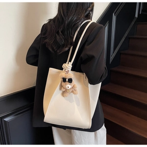 Detail of white lychee leather tote bag with braided straps and brown plush bear charm