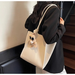 Detail of beige litchi grain tote bag with knotted strap and plush bear charm