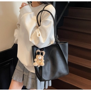 Detail of black pebbled leather tote bag with knotted shoulder strap and bear charm