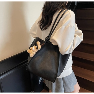 Close-up of black lychee leather tote bag with knotted shoulder straps and bear charm