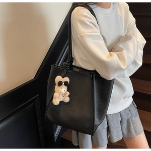 Detail of black pebbled leather tote bag with a beige plush bear charm decoration