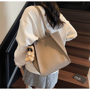 Close-up of textured grey-brown leather tote bag with knotted handle and plush bear charm