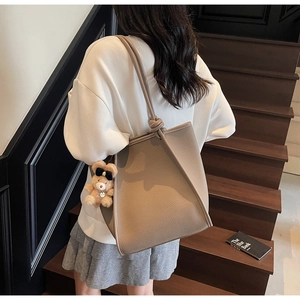 Close-up of khaki pebbled leather tote bag with knotted strap and cute bear charm