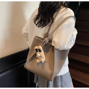 Detail of taupe pebbled leather tote bag with knot shoulder strap and plush bear charm