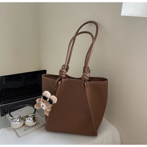 Close-up of brown lychee leather tote bag with knotted handle and plush bear charm detail