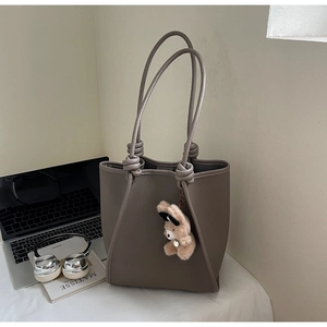 Detail of grey-brown lychee grain leather tote bag with double knotted straps and bear charm
