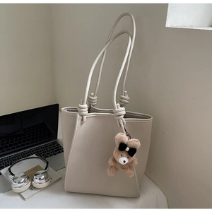 Detail of beige tote bag with pebbled leather texture and cute brown plush bear charm