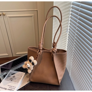 Detail of brown lychee leather tote bag featuring knot straps and a cute teddy bear charm
