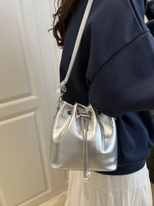 Silver metallic bucket bag with pearl drawstring and leather strap shown in use