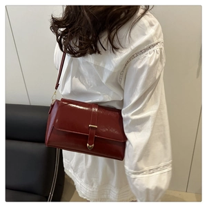 Detail of glossy dark red shoulder bag with gold heart clasp and premium leather finish