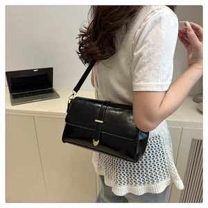 Detail of black patent leather messenger bag with gold heart-shaped buckle closure