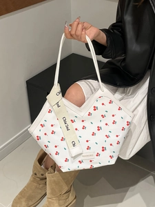 Minimalist white tote bag with red cherry print and decorative strap shown on model