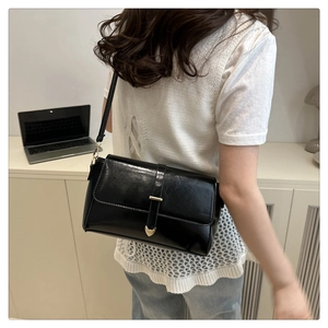Detail of a black glossy crossbody bag with gold metal tip and adjustable strap
