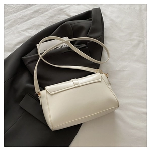 Detail of white faux leather crossbody bag with gold hardware on minimalist background