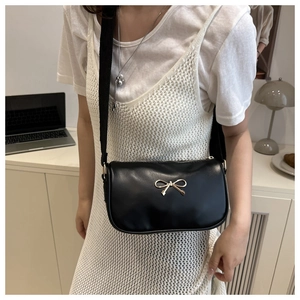 Black leather crossbody bag with golden bow buckle shown on a lifestyle model
