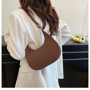 Detail view of dark brown crescent bag with pebble leather texture on white blazer