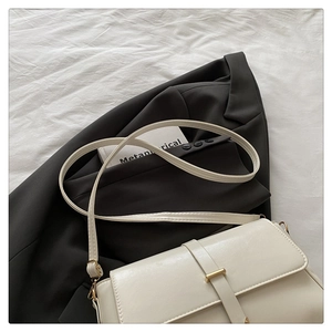 Detail of a creamy white crossbody bag with gold buckle on a minimalist textured surface