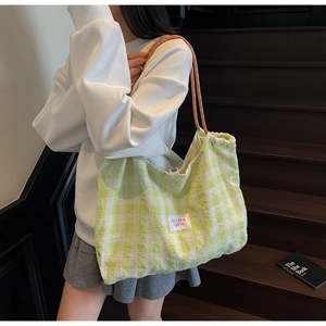 Close-up of green and white plaid woven tote bag with orange rope strap on a wooden stair