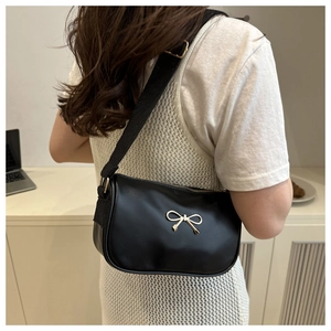 Detail of black leather underarm bag featuring a golden bow buckle and wide shoulder strap