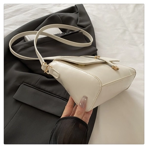 Detail of minimalist beige crossbody square bag with gold buckle on grey blazer