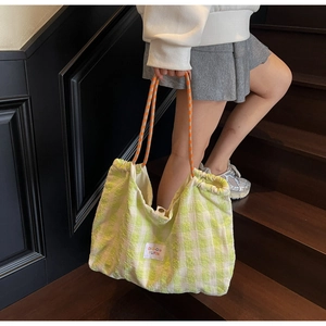 Detail of the yellow checkered tote bag with orange braided rope handles in a street setting