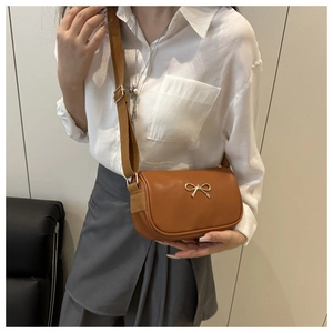 Detailed shot of brown faux leather crossbody bag featuring a gold bow and wide fabric strap