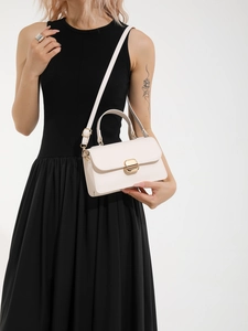 Elegant cream-colored leather crossbody bag with gold buckle on a black dress model