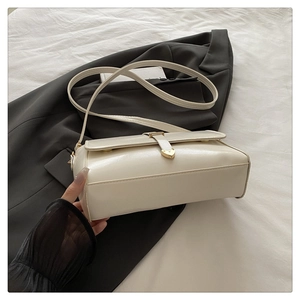 Detail of cream white crossbody bag featuring a golden heart-shaped metal buckle closure