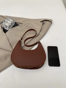 Close-up of dark brown crescent shoulder bag with lychee grain texture and metal buckle