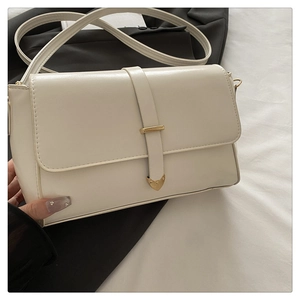 Detail of minimalist cream leather crossbody bag featuring gold heart hardware and strap