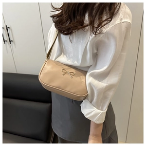 Detail of elegant beige leather handbag with golden bow accent and wide fabric strap