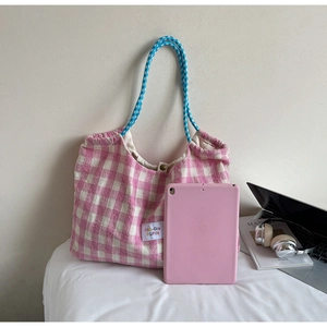Detail of pink plaid tote bag with woven handles and fabric label on a white surface