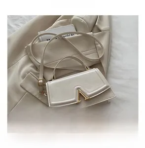 Close-up of cream white leather handbag with V-shaped gold metal lock and shoulder strap