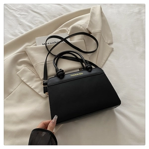 Detail of black leather handbag featuring knotted handle and gold logo on minimalist texture