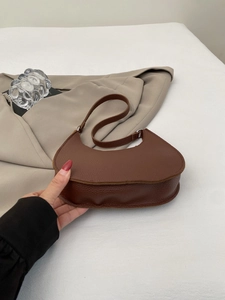 Detail of a brown leather crescent moon bag featuring a clear pebbled texture and sleek design