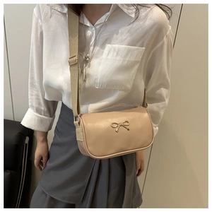 Close-up of beige crossbody camera bag with golden bow and adjustable strap