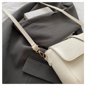 Close-up of golden strap hooks and fine leather texture on a minimalist white handbag