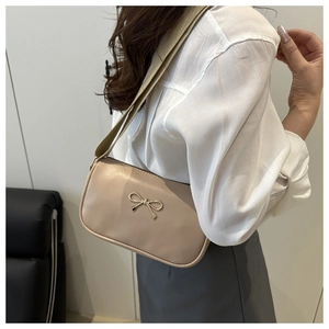 Detail of light apricot handbag featuring a decorative metal bow and wide fabric strap