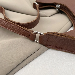 Close-up of brown litchi pattern leather bag with silver metal rings and fine stitching