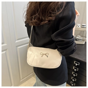 Détail d'un sac bandoulière beige crème avec un nœud doré porté par un mannequin
