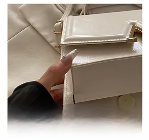 Detailed shot of white leather crossbody bag with V-shaped gold metal clasp and fine stitching